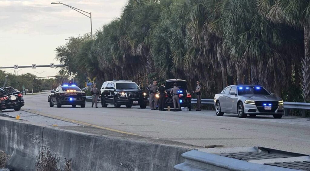 Florida Highway Patrol officers investigating a fatal tractor-trailer crash on I-95 northbound off-ramp to Palm Beach Lakes Boulevard in West Palm Beach, with multiple patrol cars and flashing lights on the highway shoulder